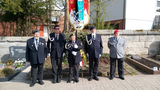 Personen in Vereinskleidung und Uniform vor einem Grab: Die Abordnung der SRK Zirndorf auf dem Friedhof Cadolzburg